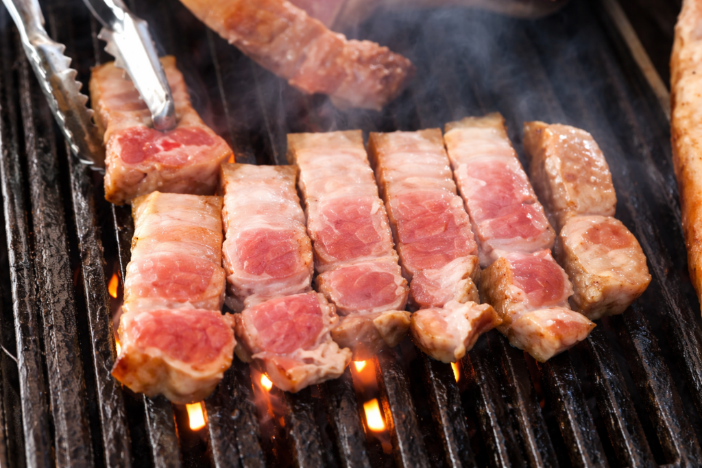 Cut pork belly pieces grilling on a barbecue grate.
