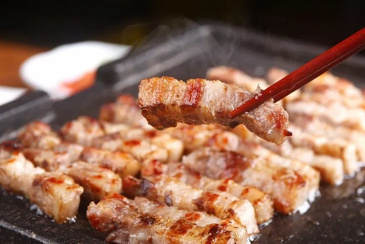 Grilled Korean pork belly pieces being picked up with chopsticks