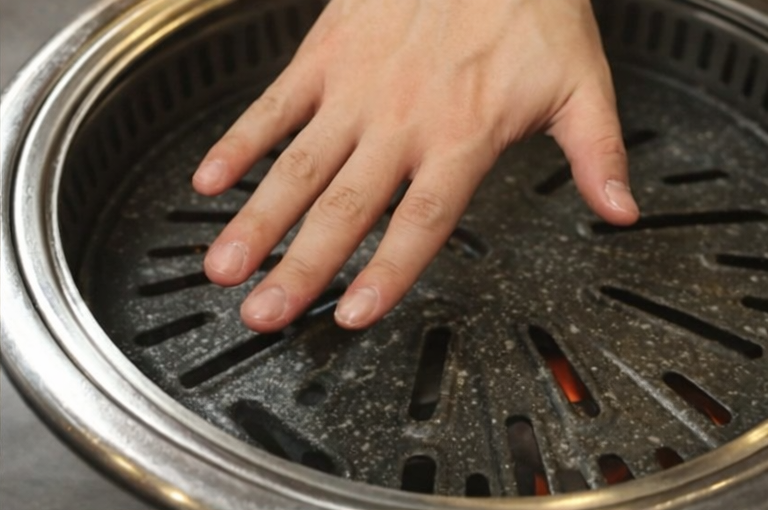 Hand checking the heat of a Korean BBQ grill plate before grilling beef