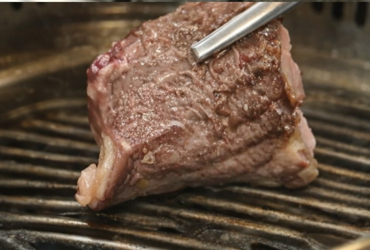 Juicy Korean BBQ beef held with chopsticks, revealing a medium-rare interior and visible marbling