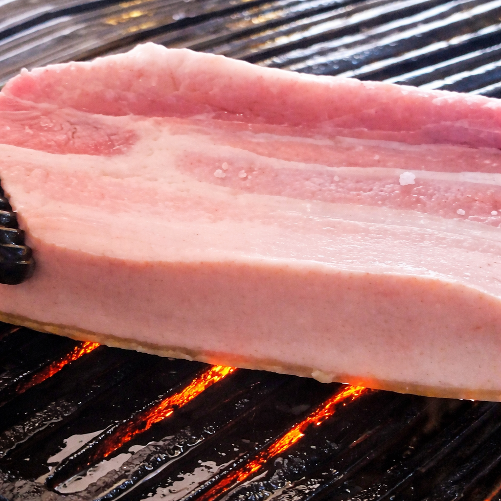 Pork belly grilling on a BBQ grate, showing the surface color changing about 1 mm as it cooks.