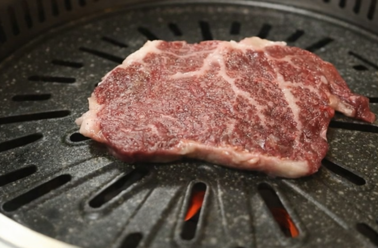 Raw marbled beef placed on a Korean-style grill plate over high heat, ready for grilling